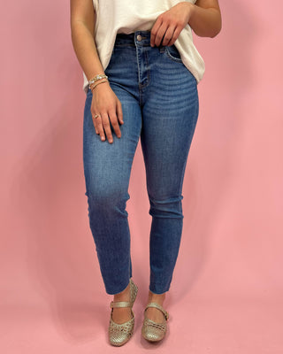 Person wearing blue jeans and a white top on a pink background