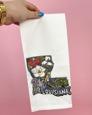 White towel with Louisiana-themed design held by a hand against a pink background