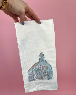 Hand holding a white towel with a blue church design against a pink background