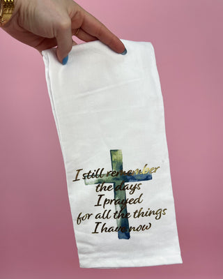 White towel with a cross and text held by a hand against a pink background