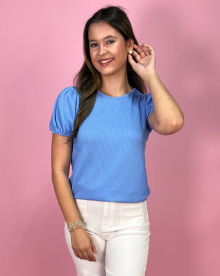 Woman wearing a blue top and white pants against a pink background
