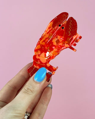 Hand holding a red and orange lobster-shaped object against a pink background