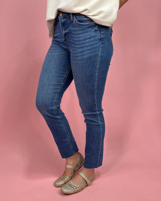 Person wearing blue jeans and gold sandals on a pink background