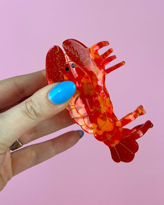 Hand holding a red lobster comb against a pink background