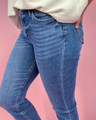 Person wearing blue jeans against a pink background