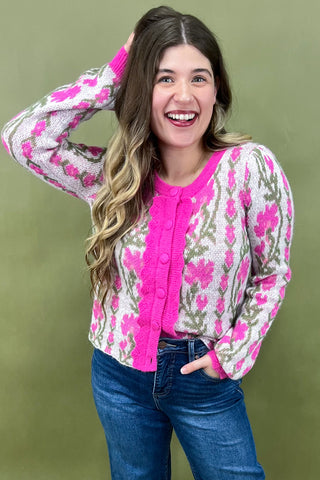 Woman wearing a pink floral cardigan over a pink shirt with blue jeans on a green background