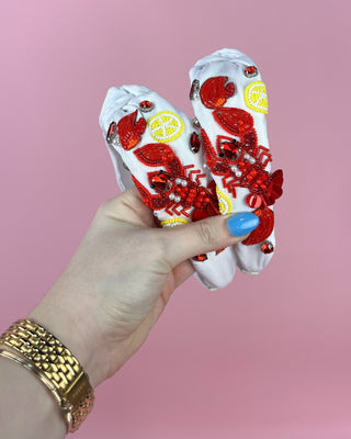 Hand holding a pair of white headband  with red crawfish designs against a pink background