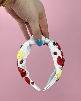 Hand holding a pair of white headband with red crawfish designs against a pink background