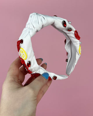 Hand holding a pair of white headband with red crawfish designs against a pink background