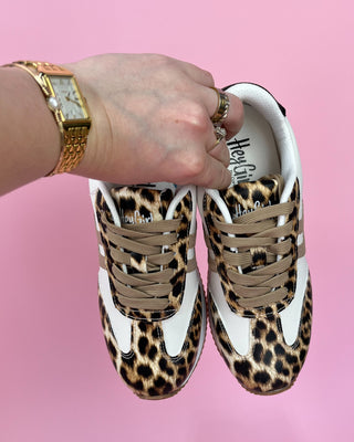 Leopard print sneakers with a hand holding them on a pink background