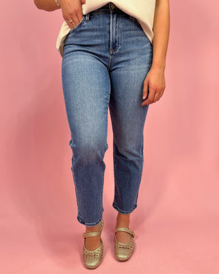 Person wearing blue jeans and gold sandals on a pink background