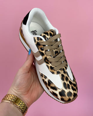 Leopard print sneaker with white sole held by a hand against a pink background