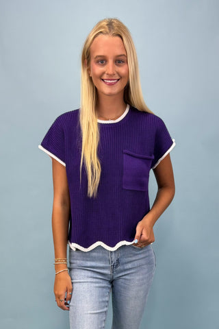 Woman wearing a purple textured top with white trim against a plain background