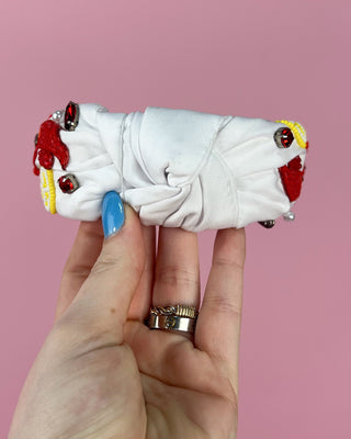 Hand holding a pair of white headband with red crawfish designs against a pink background