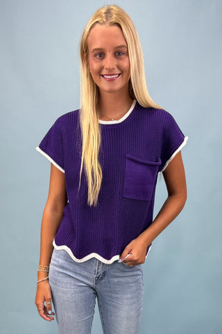Woman wearing a purple textured top with a white trim against a gray background