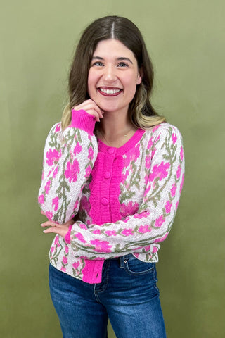 Woman wearing a pink floral cardigan over a pink shirt with blue jeans on a green background