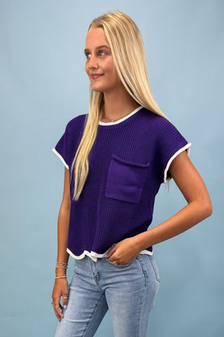 Woman wearing a purple top with a pocket and light blue jeans against a light blue background
