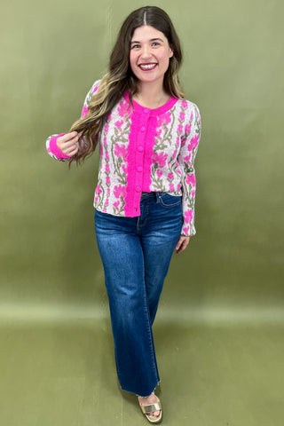 Woman wearing a floral blouse with pink accents and blue jeans on a green background