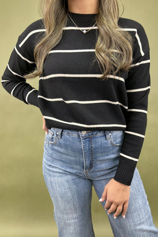 Person wearing a black and white striped sweater and blue jeans on a beige background