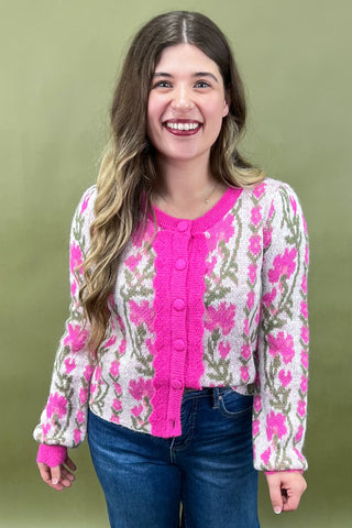 Woman wearing a floral cardigan with pink trim against a green background