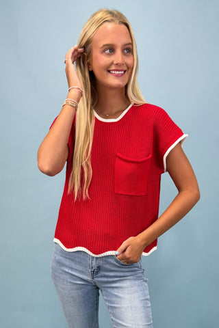 Woman wearing a red top with white trim against a light blue background
