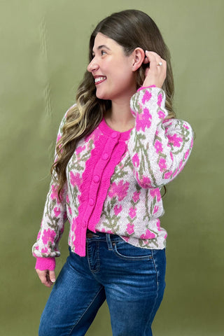 Woman wearing a floral cardigan over a pink shirt with blue jeans against a green background