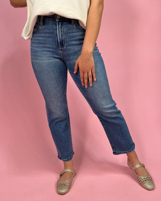 Person wearing blue jeans and a white top on a pink background