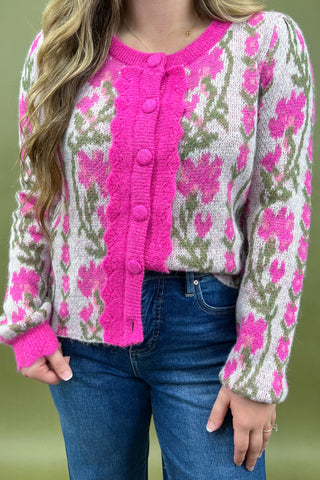 Person wearing a pink and floral patterned cardigan with blue jeans on a green background
