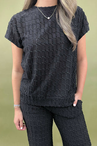 Person wearing a textured black top and pants against a green background