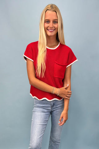 Woman wearing a red top with white trim and light blue jeans against a gray background