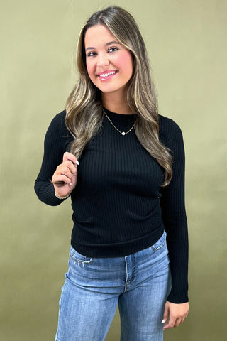 Woman wearing a black ribbed sweater and blue jeans against a beige background