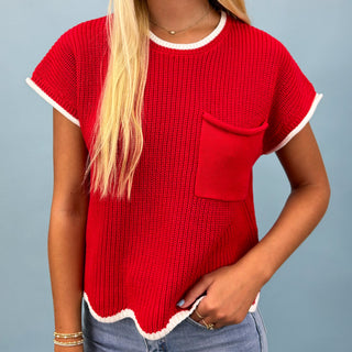 Person wearing a red knitted top with white trim on a gray background