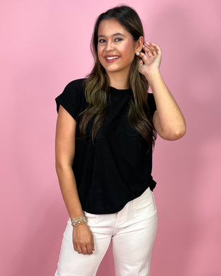 Woman wearing a black top and white pants against a pink background