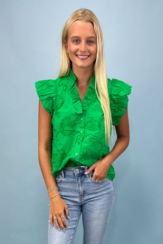 Woman wearing a green ruffled blouse and blue jeans against a light gray background