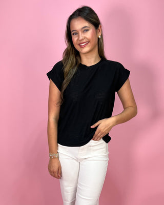Woman wearing a black t-shirt and white pants against a pink background