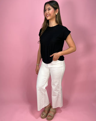 Woman wearing a black top and white pants against a pink background