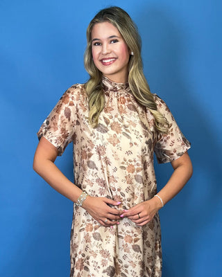A woman modeling a short-sleeve, high-neck midi dress with a brown and beige floral pattern
