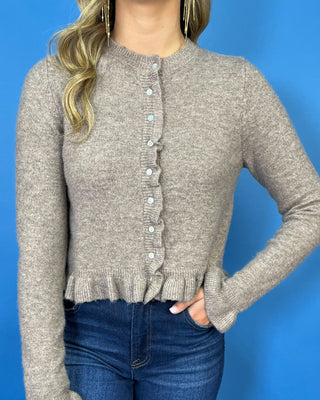 Taupe knit cardigan with delicate ruffle trim, pearl-style buttons, ruffled hem, and feminine flared cuffs.