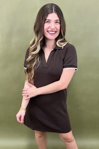 Woman wearing a brown dress with white trim against a green background