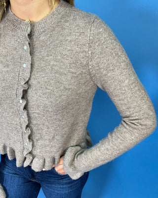 Taupe knit cardigan with delicate ruffle trim, pearl-style buttons, ruffled hem, and feminine flared cuffs.