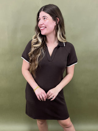 Woman wearing a brown dress with white trim against a green background