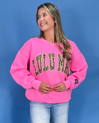 Woman wearing a pink sweatshirt with leopard print letters against a blue background