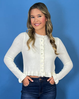 Ivory knit cardigan with ruffle trim, pearl-style buttons, ruffled hem, and feminine flared cuffs