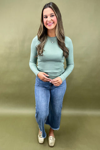 Woman wearing a green ribbed sweater and blue jeans against a beige background