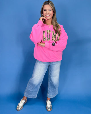 Woman wearing a pink sweatshirt with leopard print text and blue jeans on a blue background
