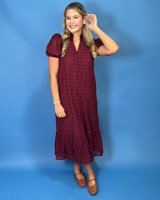 A woman modeling a short-sleeve burgundy eyelet lace midi dress with puff sleeves