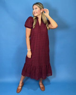 A woman modeling a short-sleeve burgundy eyelet lace midi dress with a ruffled hem