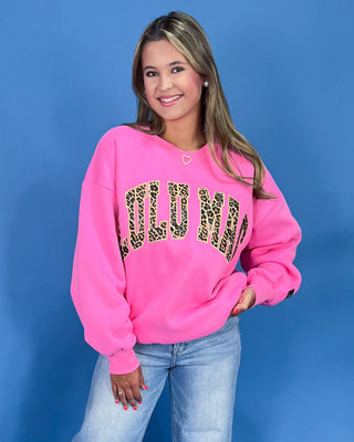 Person wearing a pink sweatshirt with leopard print text against a blue background
