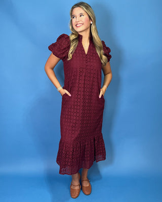 A woman modeling a burgundy crochet midi dress with puff sleeves and a ruffled hem