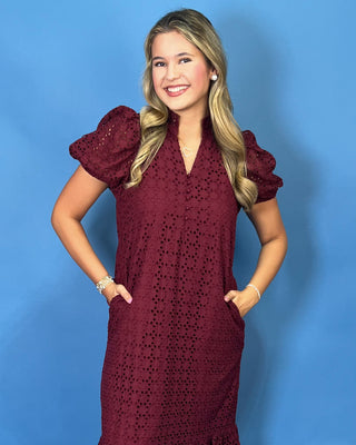A woman modeling a short-sleeve burgundy eyelet lace midi dress with puff sleeves
